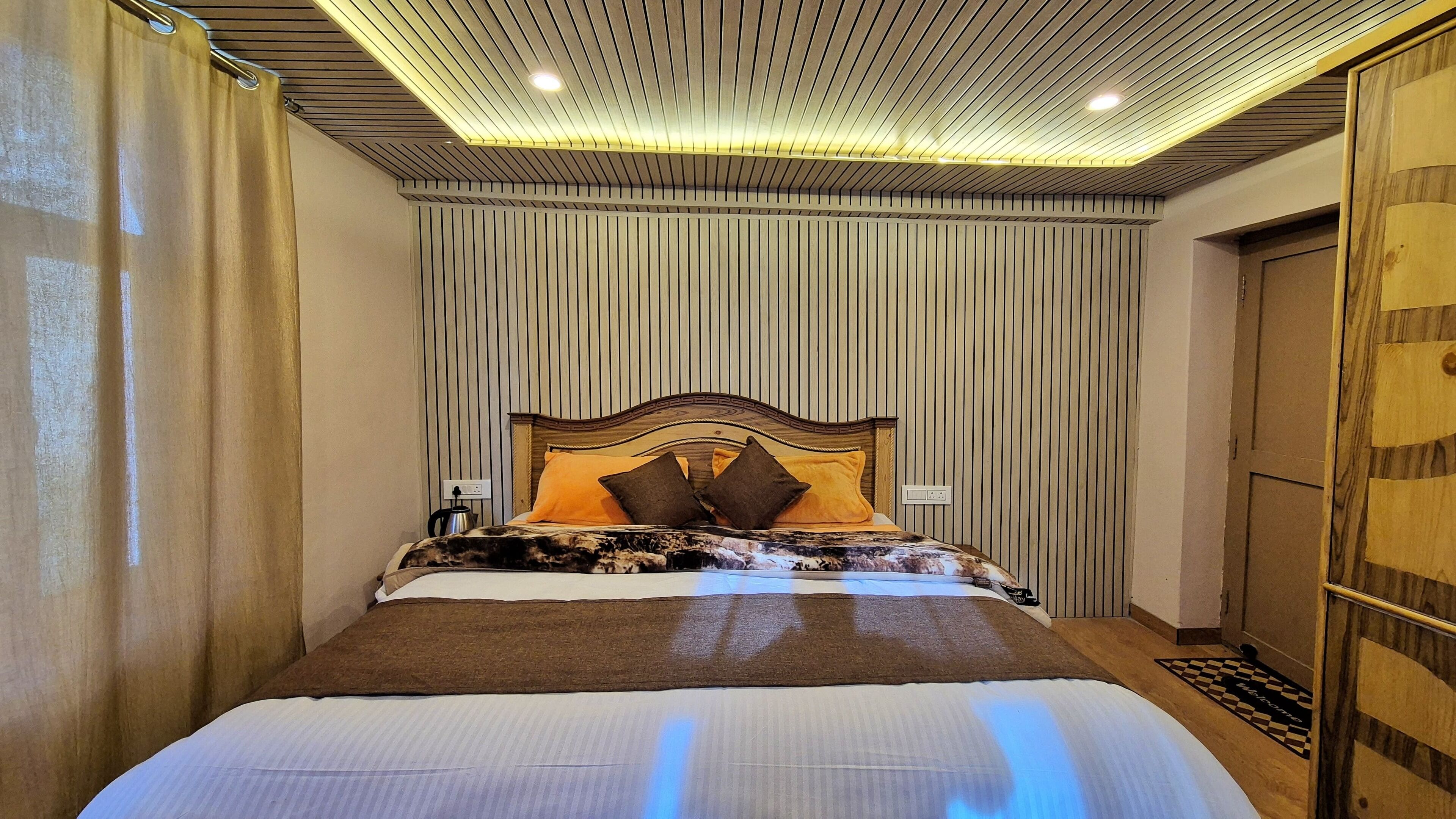 A modern hotel room with a large bed, wooden headboard, and a ceiling with linear lighting.