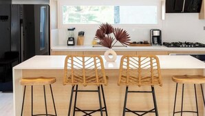 Una cucina moderna con un'isola centrale, due sgabelli in vimini, una macchina per il caffè e un piano cottura a gas.