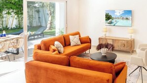 Un soggiorno moderno con un ampio divano arancione, un tavolino da caffè e una TV fissata al muro.