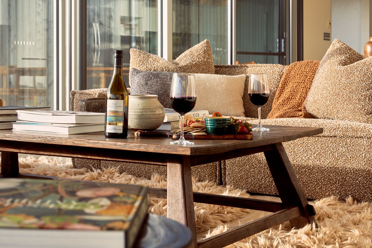 A cozy living room with a sofa, a coffee table, a wine bottle, glasses, and a bowl of fruit.