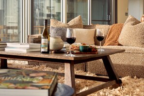 A cozy living room with a sofa, a coffee table, a wine bottle, glasses, and a bowl of fruit.