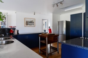 Eine moderne Küche mit dunkelblauen Schränken, einem Edelstahlkühlschrank, einem Holzwagen und einem gerahmten Bild an der Wand.