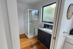 A modern bathroom with a glass shower enclosure, a sink with a granite countertop, and a window above the sink. - Forest Edge - Breathtaking Views of the Hazards (Coles Bay)