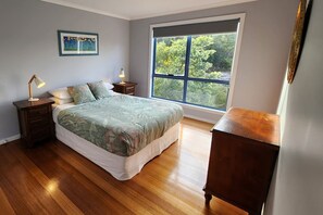 Ein Schlafzimmer mit großem Fenster, einem Bett, einem Nachttisch und einer Kommode.