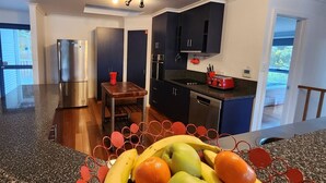 A modern kitchen with a stainless steel refrigerator, a wooden table, and a fruit bowl. - Forest Edge - Breathtaking Views of the Hazards (Coles Bay)
