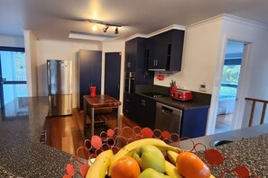 A modern kitchen with a stainless steel refrigerator, a wooden table, and a fruit bowl. - Forest Edge - Breathtaking Views of the Hazards (Coles Bay)