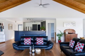 A modern living room with a black leather sofa, a wooden coffee table, and a dining area with a blue countertop and stainless steel appliances. - Forest Edge - Breathtaking Views of the Hazards (Coles Bay)