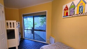 A room with a bunk bed, a large sliding glass door leading to an outdoor area, and a wall with colorful artwork. - Forest Edge - Breathtaking Views of the Hazards (Coles Bay)