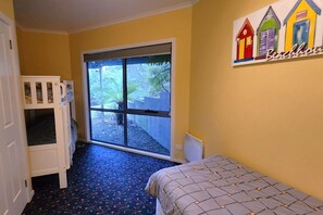 A room with a bunk bed, a large sliding glass door leading to an outdoor area, and a wall with colorful artwork. - Forest Edge - Breathtaking Views of the Hazards (Coles Bay)