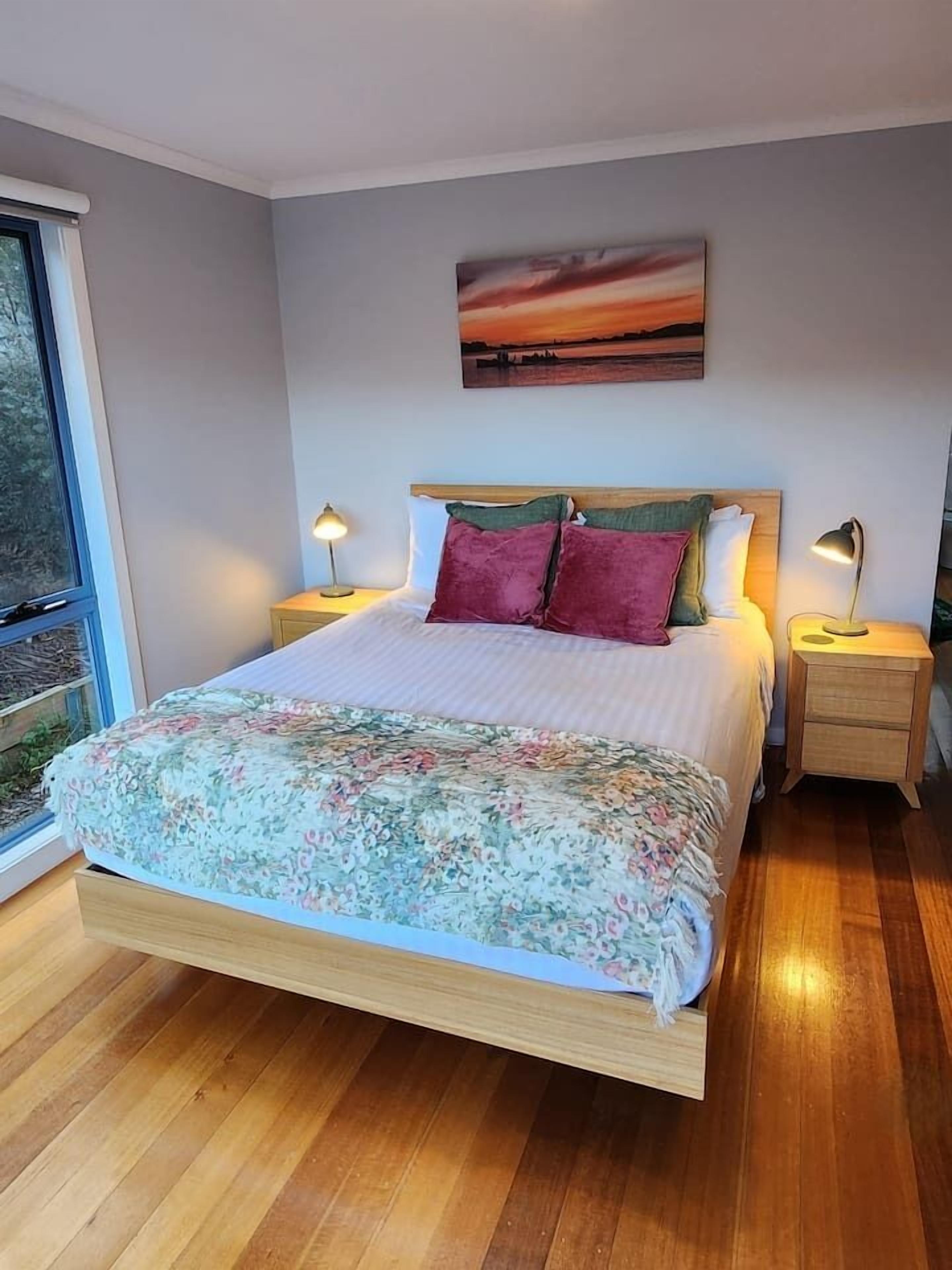 Un dormitorio con una cama grande, dos mesitas de noche, un ventanal y un cuadro en la pared.