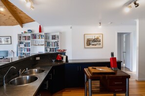 A modern kitchen with a granite countertop, stainless steel sink, and a wooden island with a cutting board and knife block. - Forest Edge - Breathtaking Views of the Hazards (Coles Bay)