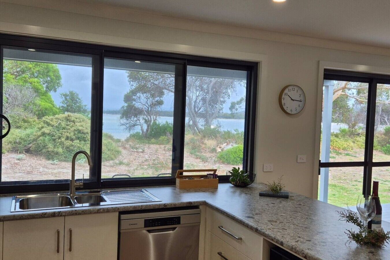 A kitchen with a view of a lake, a clock on the wall, and a dishwasher.
