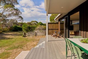 A wooden deck with outdoor seating, a fenced yard, and a building with a large window. - Joeys Place- Waterfront| Views| Sunsets @Freycinet (Coles Bay)