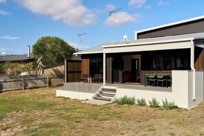 A modern two-story house with a covered patio area, a staircase leading to the upper level, and a fenced backyard. - Joeys Place- Waterfront| Views| Sunsets @Freycinet (Coles Bay)