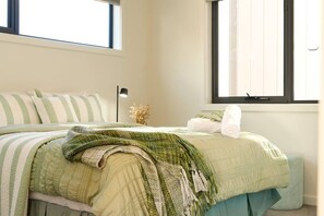 Une chambre à coucher avec un lit, des oreillers, une couverture, une lampe de chevet et une fenêtre.