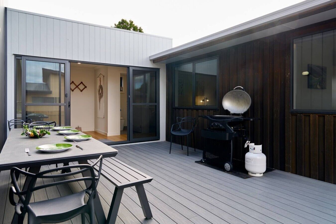 An outdoor dining area with a table set for four, a grill, and a gas cylinder.