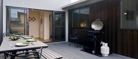An outdoor dining area with a table set for four, a grill, and a gas cylinder.