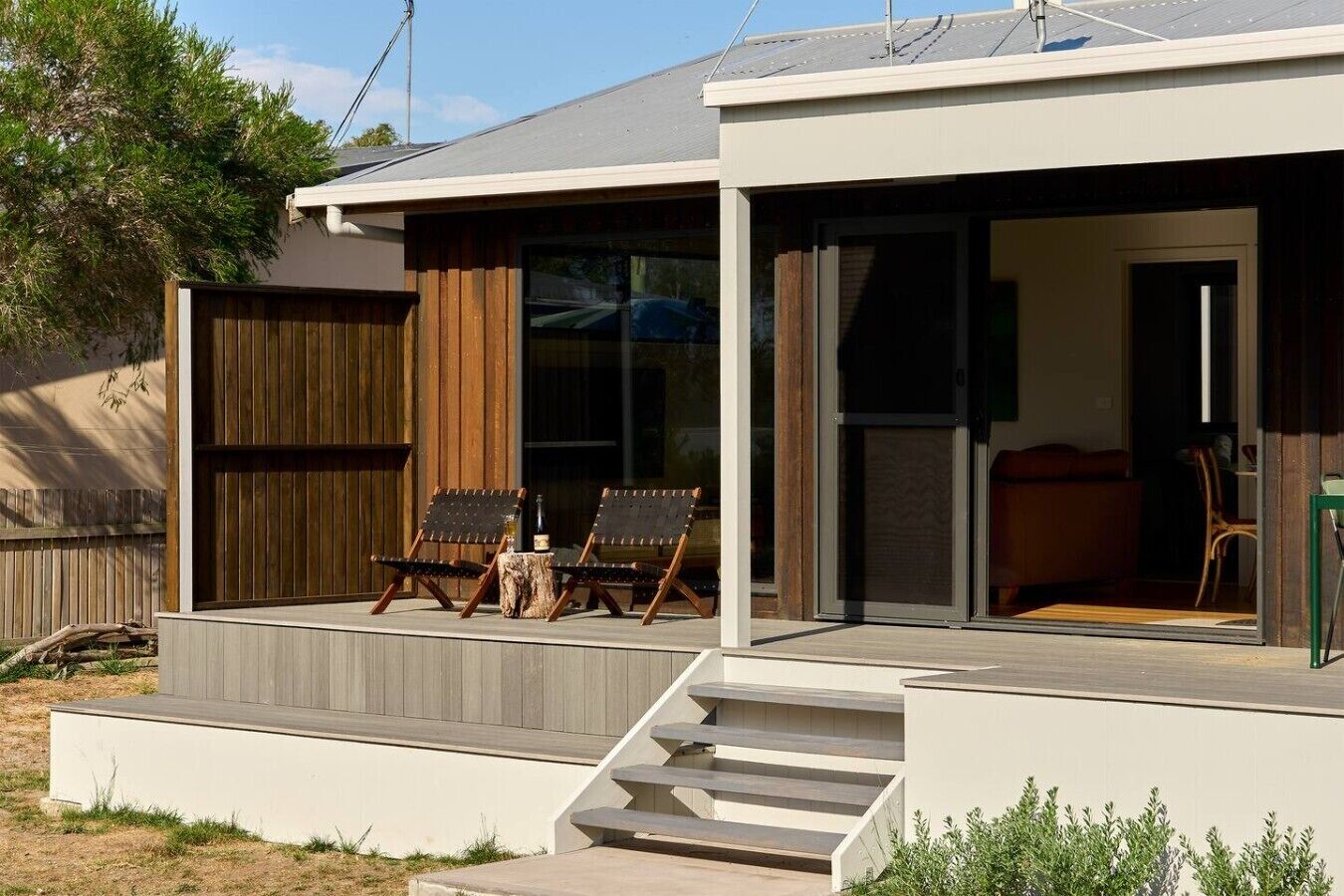 A modern house with a covered porch, two lounge chairs, and a staircase leading to the entrance.