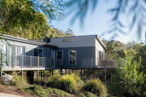 Una casa moderna de dos pisos con un balcón, rodeada de vegetación.
