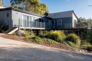 Une maison à deux étages dotée d’un espace extérieur couvert et d’un escalier menant à une terrasse.
