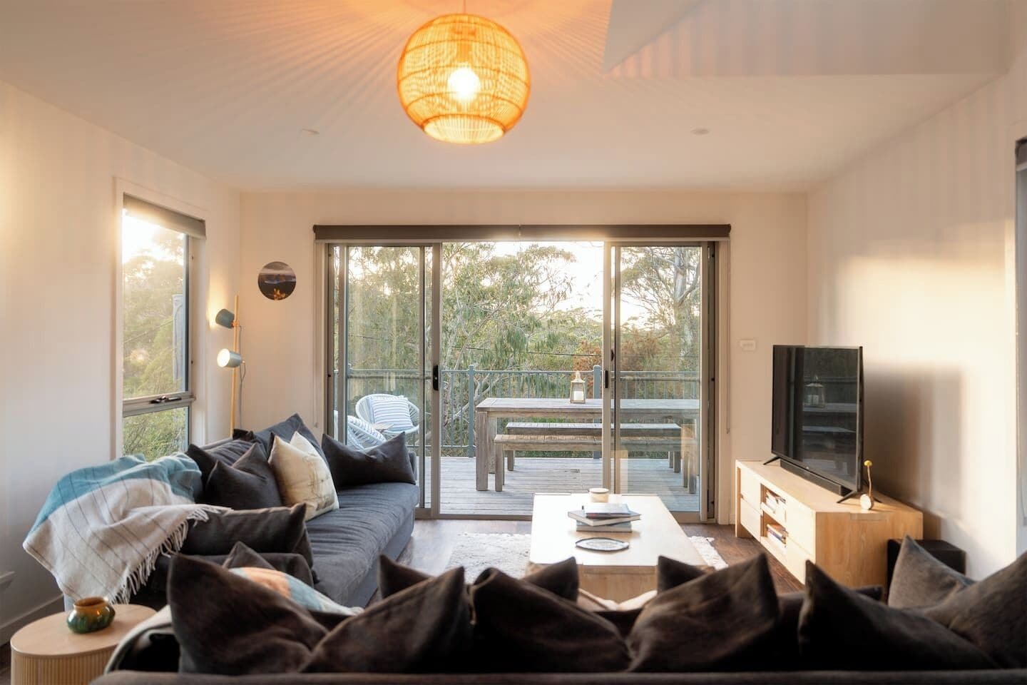 A modern living room with a sofa, a coffee table, and a television. There is a sliding glass door leading to an outdoor deck.