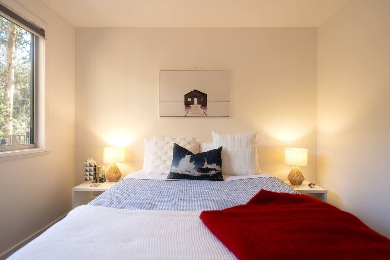 Habitación de hotel con cama, dos lámparas de noche, una ventana y un cuadro colgado en la pared.