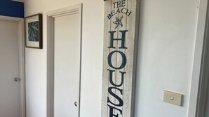 Ein Flur mit einer Tür, einem gerahmten Bild und einem vertikalen Schild mit der Aufschrift 'THE BEACH HOUSE'.