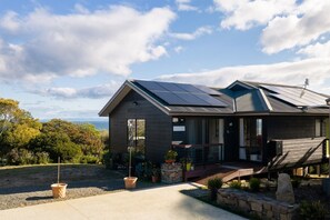 Une maison moderne dotée de panneaux solaires, d’un porche abrité et offrant une vue sur la mer.