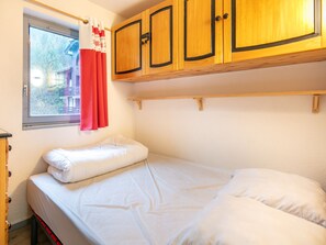 A small, single-bed room with wooden cabinets above the bed and a window with curtains. - Charming Apart for 6 Near the Slopes (Morillon)