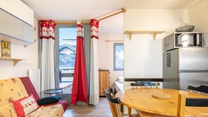 Un salon confortable avec un canapé, une table à manger avec des chaises, un coin cuisine équipé d’un réfrigérateur et d’un four à micro-ondes, et une fenêtre avec des rideaux.