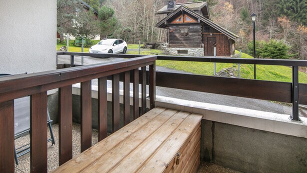 Un banc et une rambarde en bois offrent une vue panoramique sur un chalet et une voiture blanche garée dans une zone boisée.