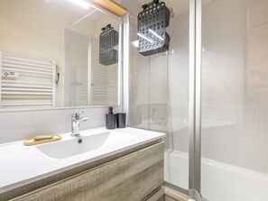 A bathroom with a white sink, a mirror, a shower with glass doors, and a wooden vanity. - Charming Apart for 6 Near the Slopes (Morillon)