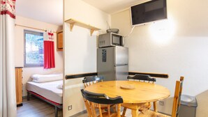 Une pièce de taille modeste comprenant un lit, une table à manger avec des chaises, un four à micro-ondes, un réfrigérateur, un téléviseur fixé au mur et une fenêtre avec des rideaux.