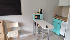 Una cocina compacta con un refrigerador color turquesa, una encimera blanca, una mesita y una silla de madera.