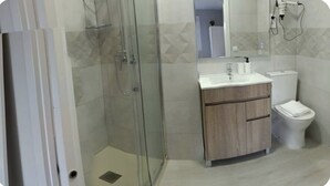 Un baño moderno con ducha de vidrio, tocador de madera, inodoro y espejo.