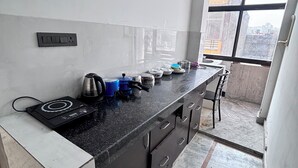 A compact kitchen with a black countertop, a built-in stove, and a window providing a view of the cityscape. - Sk Govindam (Jaipur)
