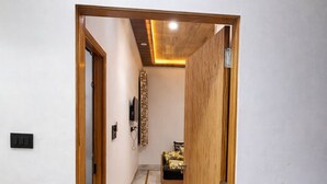 A hallway with a wooden door leading to a room with a bed and a TV. - Sk Govindam (Jaipur)