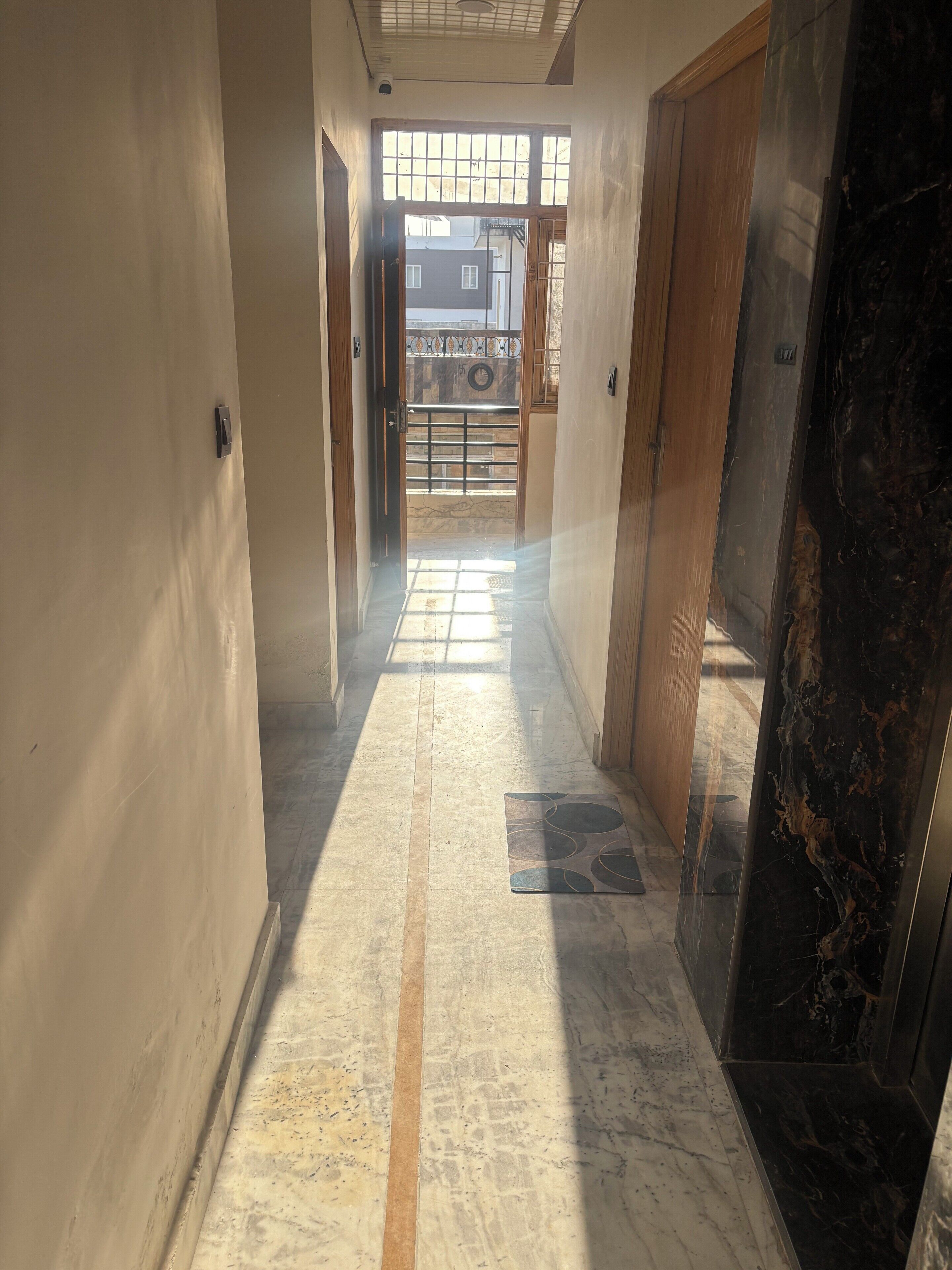 Un pasillo con suelo de baldosas, puertas de madera y vistas de un edificio a través de una ventana.