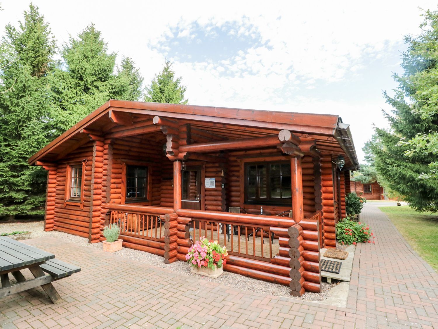 A log cabin with a porch, a picnic table, and a garden area.