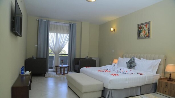 A hotel room with a large bed, a desk, a chair, a small table, and a TV mounted on the wall. - Daisy Hotel (Addis Ababa)