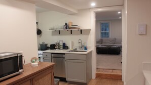 A compact kitchen with a microwave, sink, and cabinets. There is a dining area with a table and chairs visible through an open door. - 2BR/2BA in a Duplex; Private entry & free parking; Downtown Holliston (Holliston)