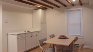 A dining area with a wooden table and chairs, a white counter with cabinets, and a window with blinds. - 2BR/2BA in a Duplex; Private entry & free parking; Downtown Holliston (Holliston)