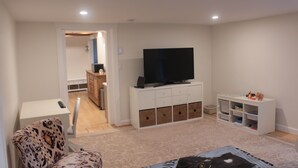 A living room with a flat-screen TV, a patterned armchair, a white cabinet with storage drawers, and a bookshelf. - 2BR/2BA in a Duplex; Private entry & free parking; Downtown Holliston (Holliston)