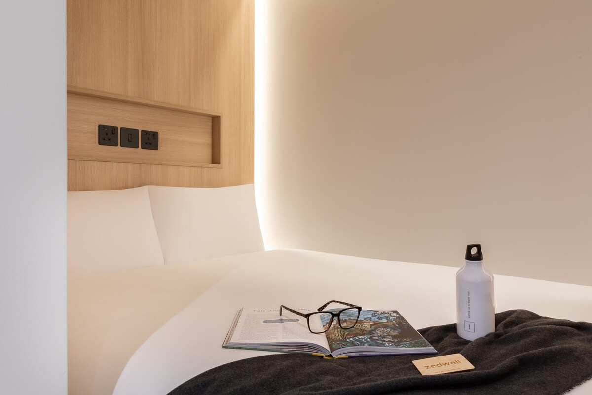 Una cama bien hecha con un libro, gafas y una botella de agua sobre una manta.
