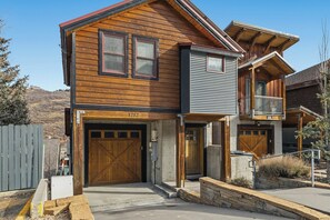 Ein zweistöckiges Holzhaus mit Garage, Balkon und einer Steinmauer.