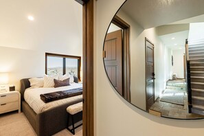 Ein Schlafzimmer mit einem großen Bett, Nachttischen, einem Spiegel und Blick ins Freie.