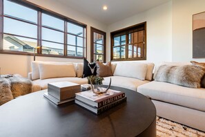 Ein modernes Wohnzimmer mit einer Couch, einem Couchtisch mit Büchern und großen Fenstern.