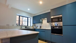 A modern kitchen with dark blue cabinets, a marble countertop, a built-in microwave, and an oven. - Courtyard View at Longford (Longford)