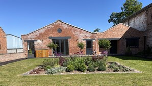 A brick building with a central entrance, a small garden with various plants, and a clear blue sky. - Courtyard View at Longford (Longford)