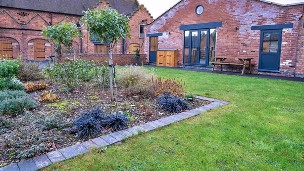 A brick building with a garden in front, a wooden bench, and a door. - Courtyard View at Longford (Longford)